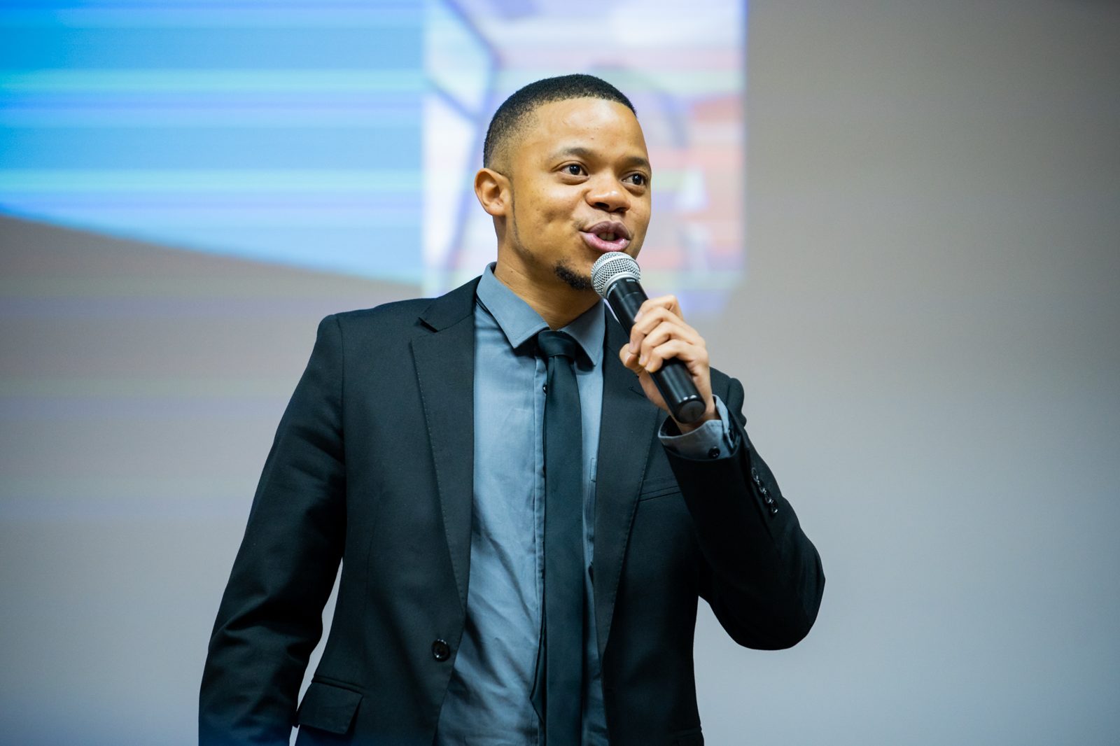 Presenter speaking with a microphone in front of the screen